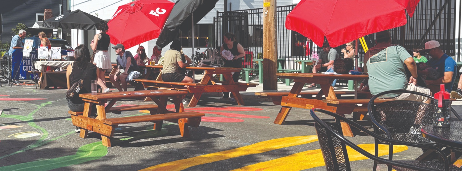 Neighbors gathered at picnic tables under red umbrellas at the Beaumont Crossing plaza