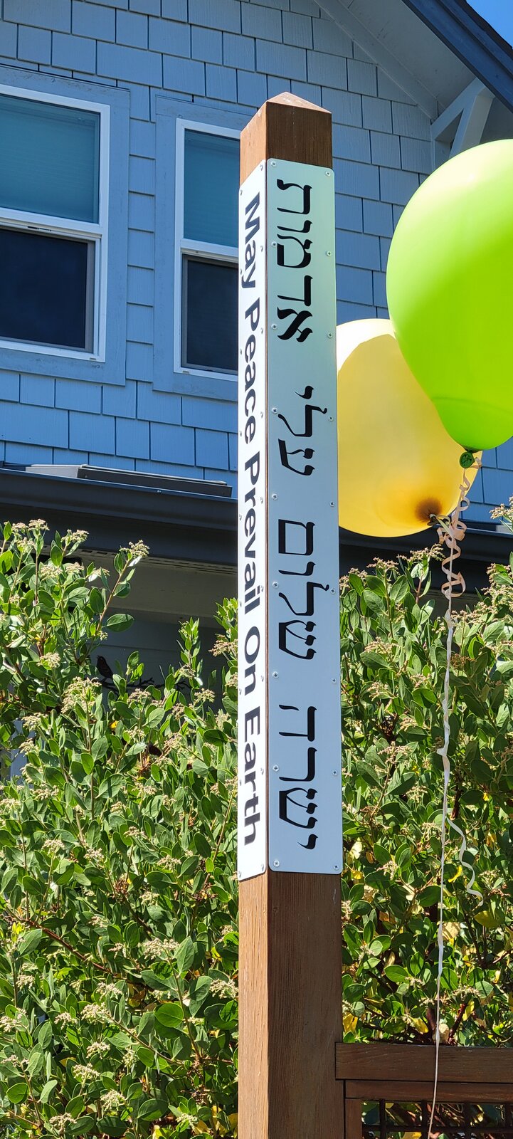 A Peace Pole reading 'May Peace Prevail On Earth' in a garden.