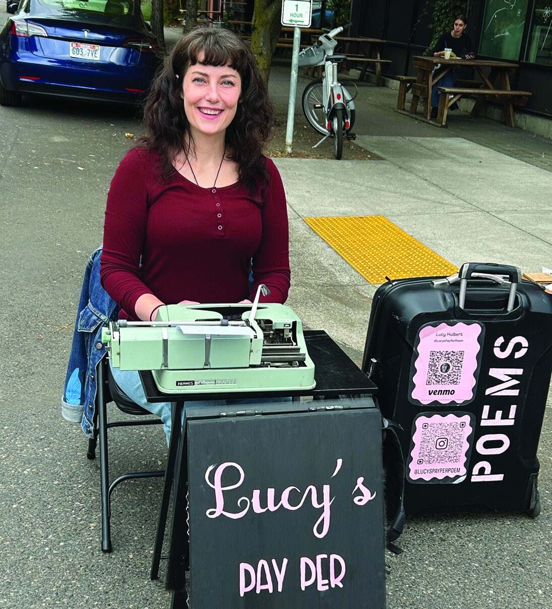 A poet, Lucy, at a typewriter with a Pay Per Poem sign.